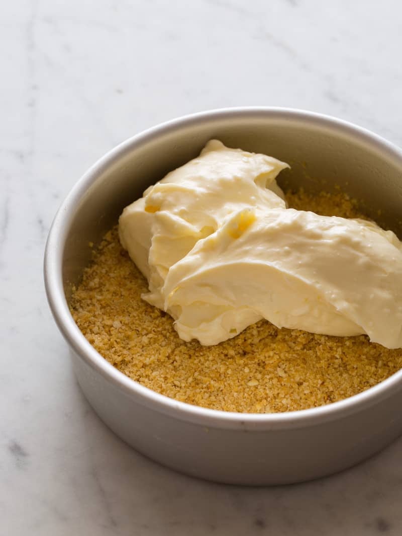 A pan with crust in the bottom and cheesecake filling ready to be spread.