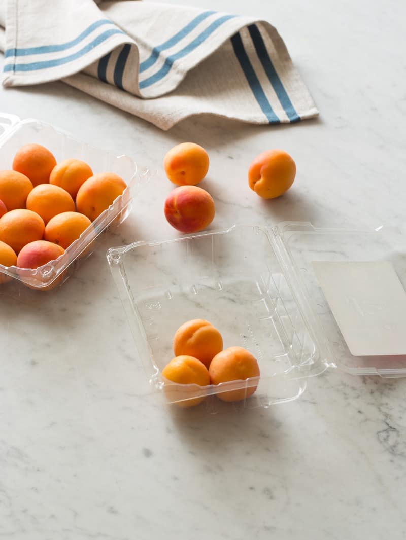 Open plastic containers of fresh apricots with linens on a marble countertop.
