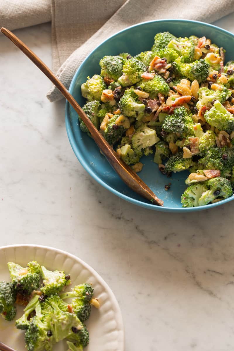 A bowl of broccoli crunch salad with a wooden spoon and some salad on a plate.