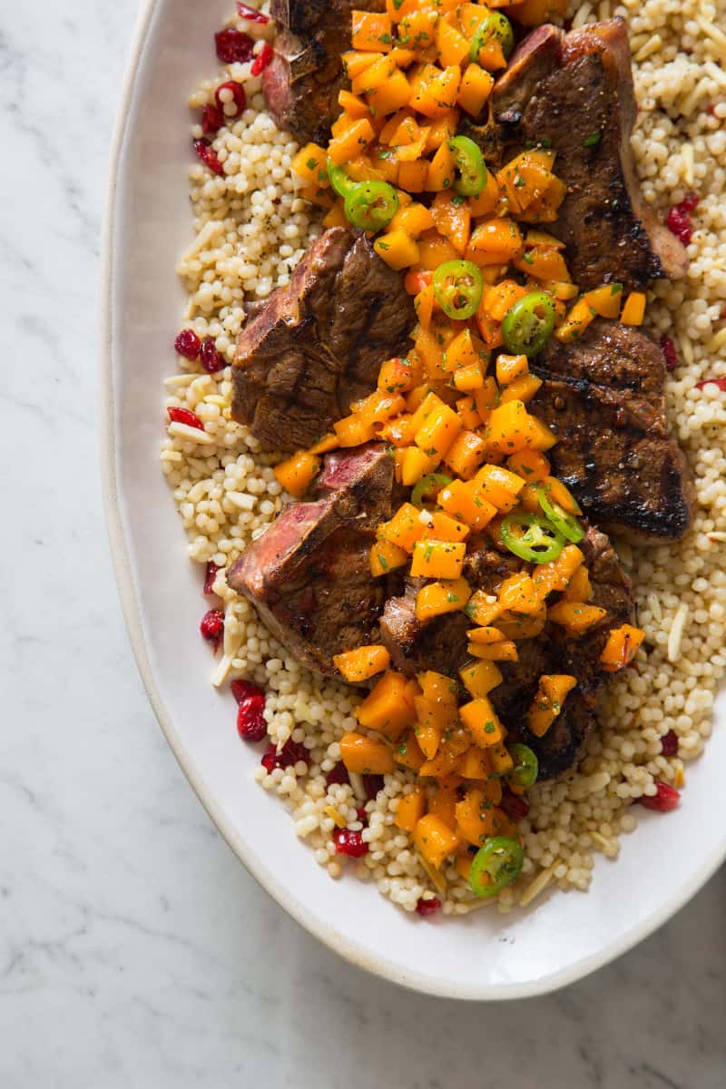 A close up of harissa grilled lamb chops with fresh apricot serrano salsa on couscous.