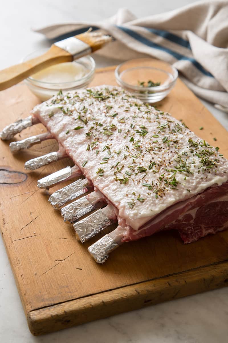 Raw rack of lamb seasoned and prepped for grilling on a wooden cutting board.