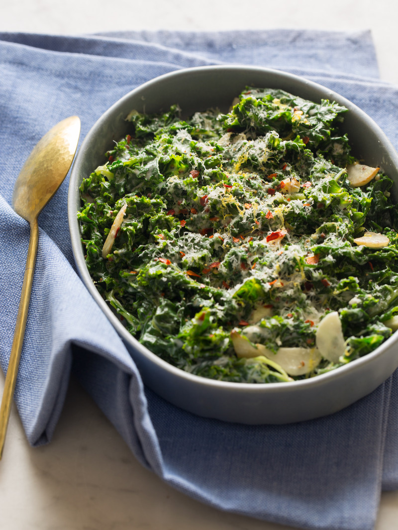 Creamed kale in a large serving dish with a spoon on a blue linen.