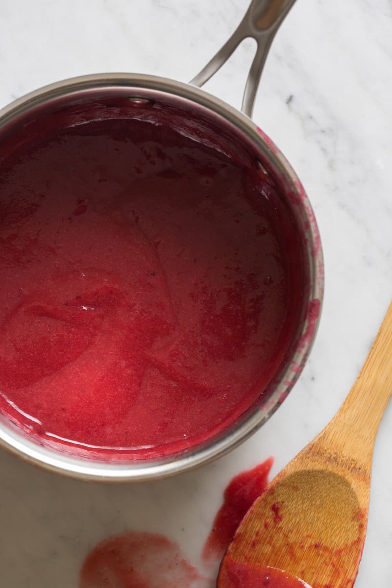A close up of sweet plum glaze in a pan next to a wooden spoon.