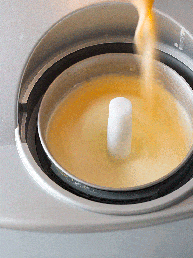 Ice cream base in an ice cream maker with cantaloupe mixture being poured in gif.