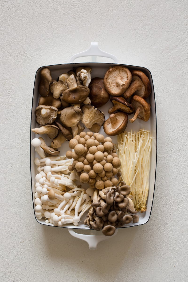 A variety of fresh mushrooms laid out in a white pan.