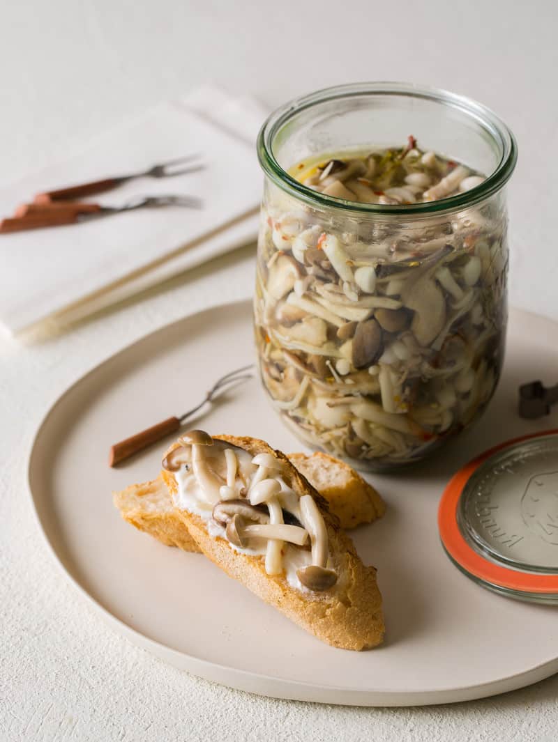 Pickled Mushrooms recipe A plate with an open jar of pickled mushrooms with some mushrooms on bread.
