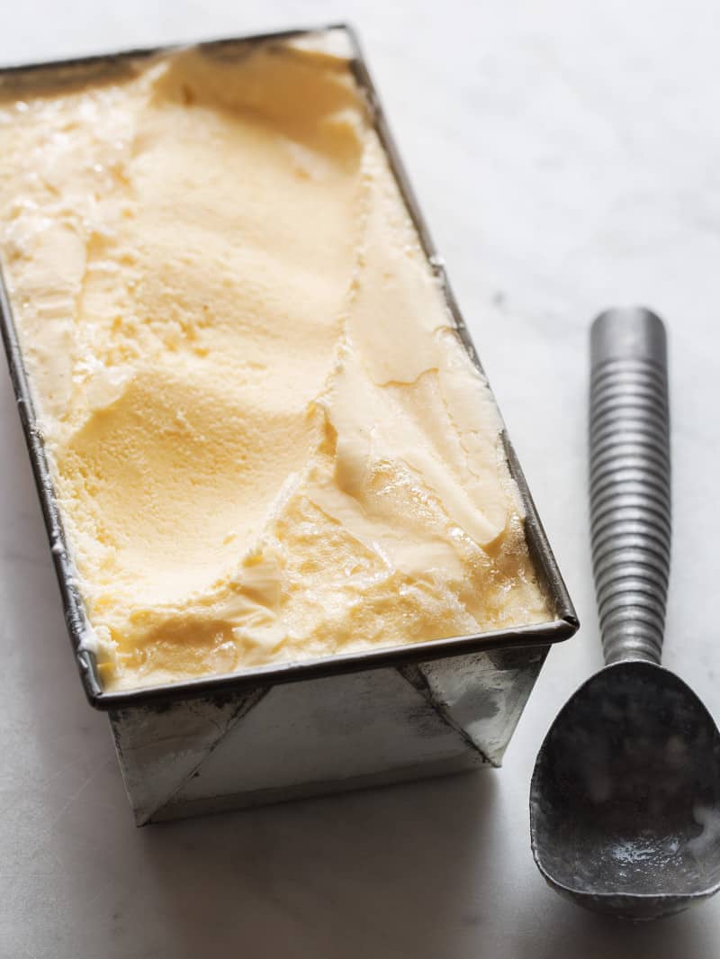 A rectangular pan of salted cantaloupe ginger ice cream with an ice cream scoop.