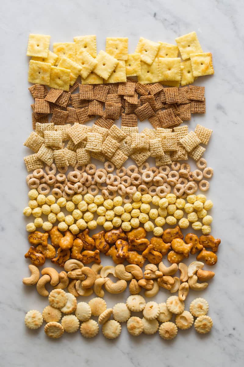 Cereals, crackers, and nuts for snack mix on a marble surface.