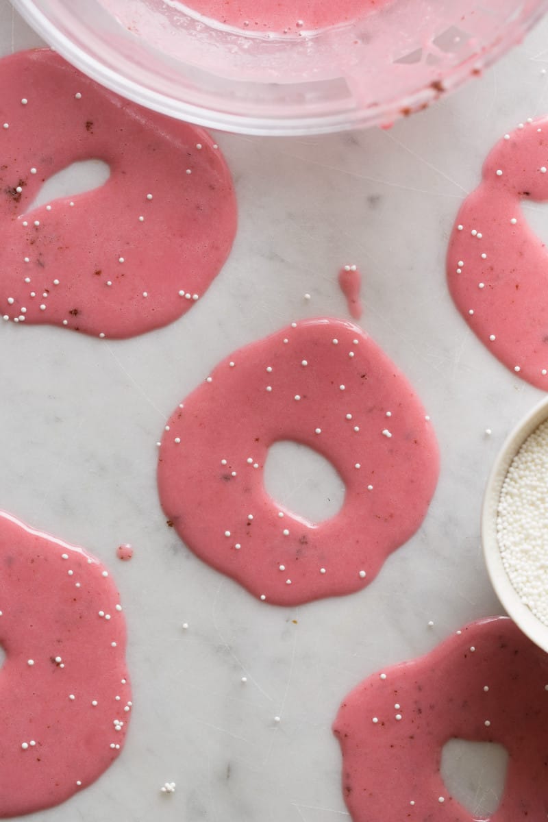 A close up of circles of sweet plum glaze and sprinkles on a marble surface.