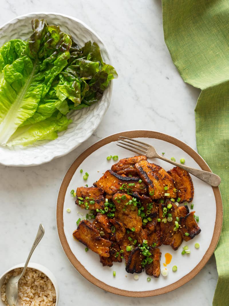 A plate of Korean style marinated spicy pork belly next to a plate of lettuce.