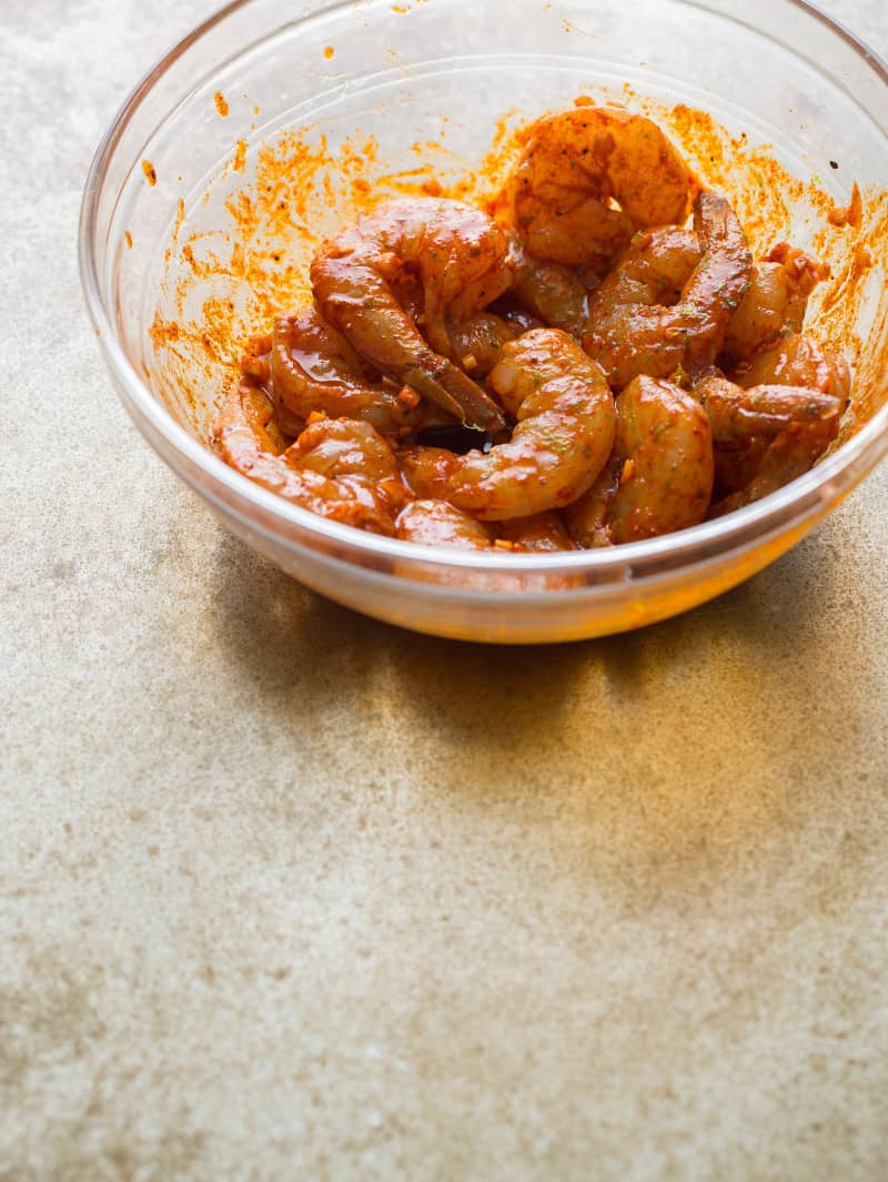 A bowl of raw shrimp mixed with spices.