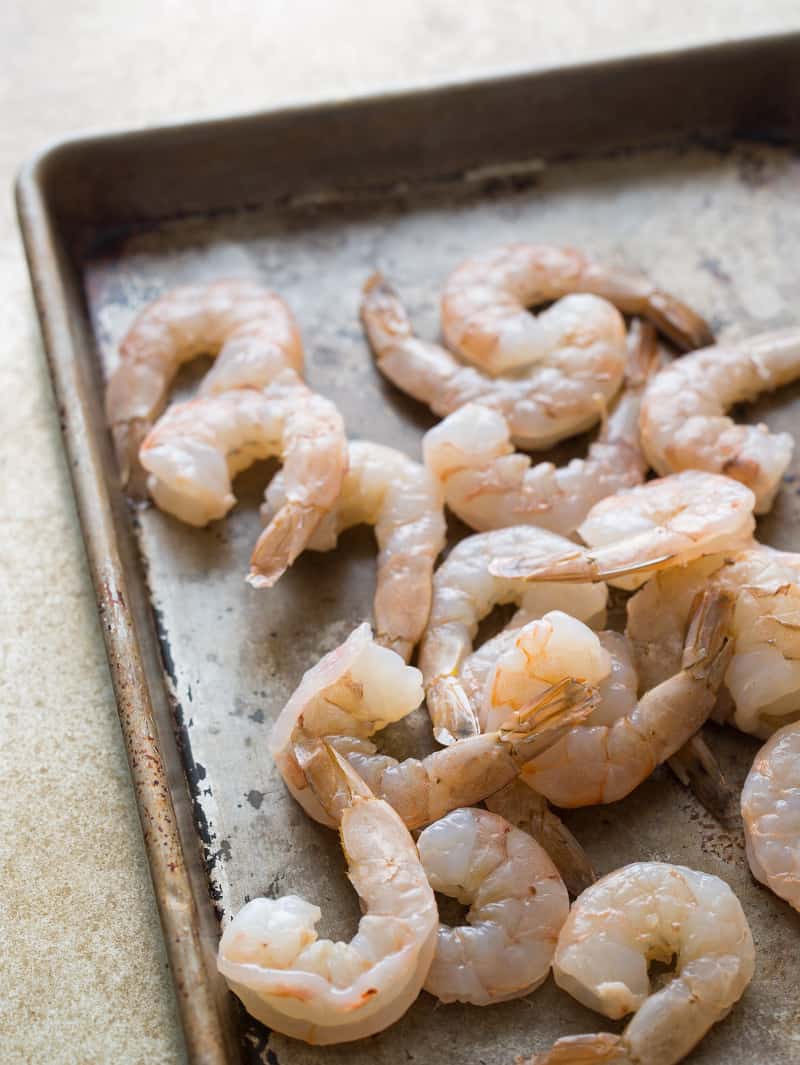 A close up of raw shrimp on a baking sheet.