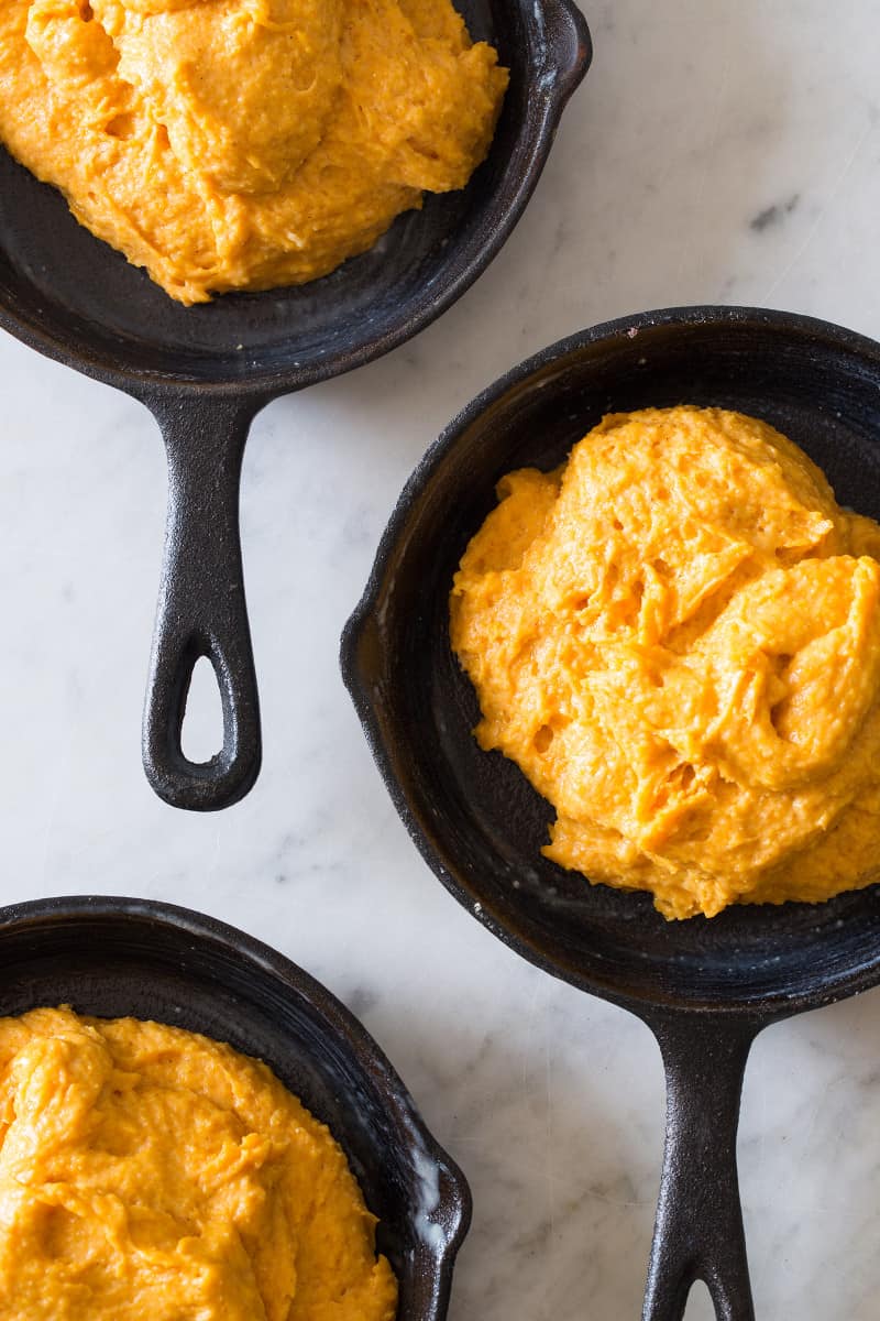 A close up of pumpkin cornbread batter in cast iron skillets.