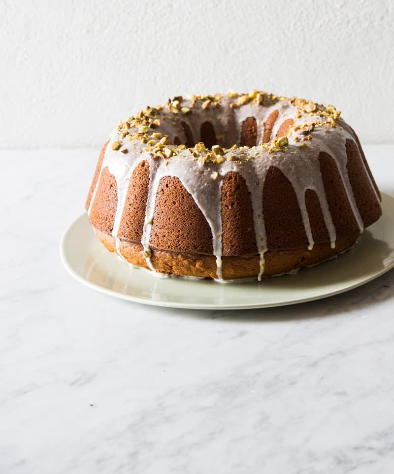 A pumpkin bundt cake topped with pistachio glaze and pistachios on a plate.