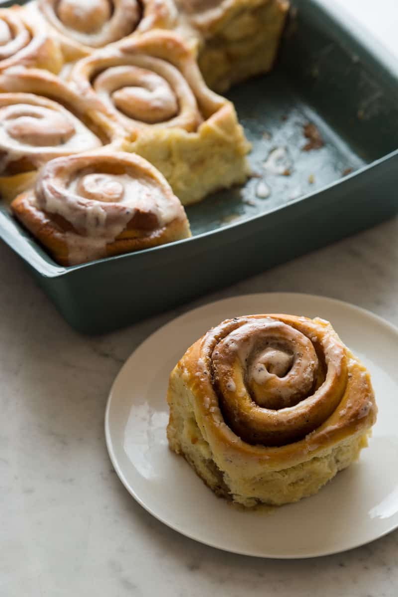 A pan of brown butter cinnamon rolls with one on a plate.