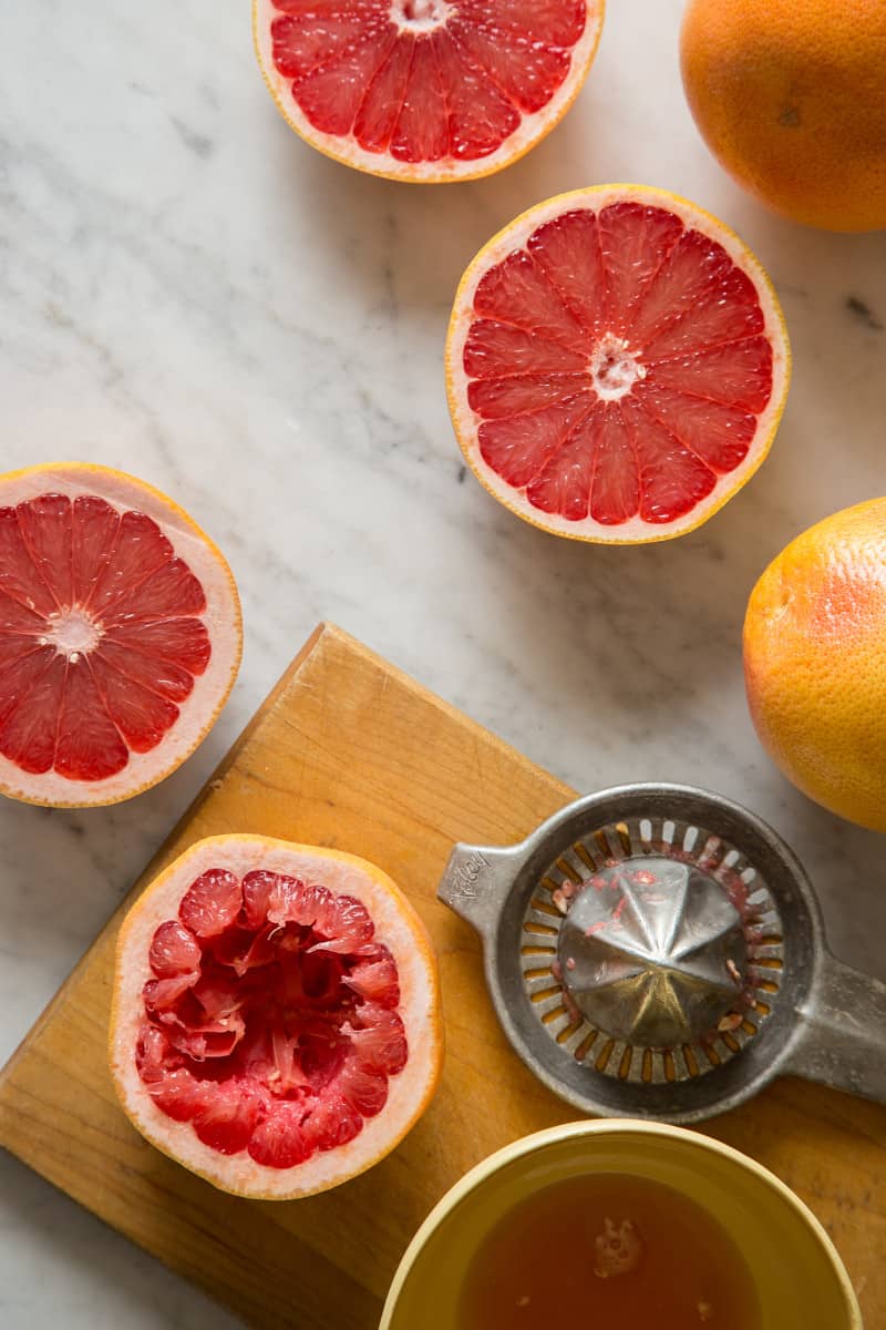 Red grapefruits cut in half, being juiced with a citrus juicer.