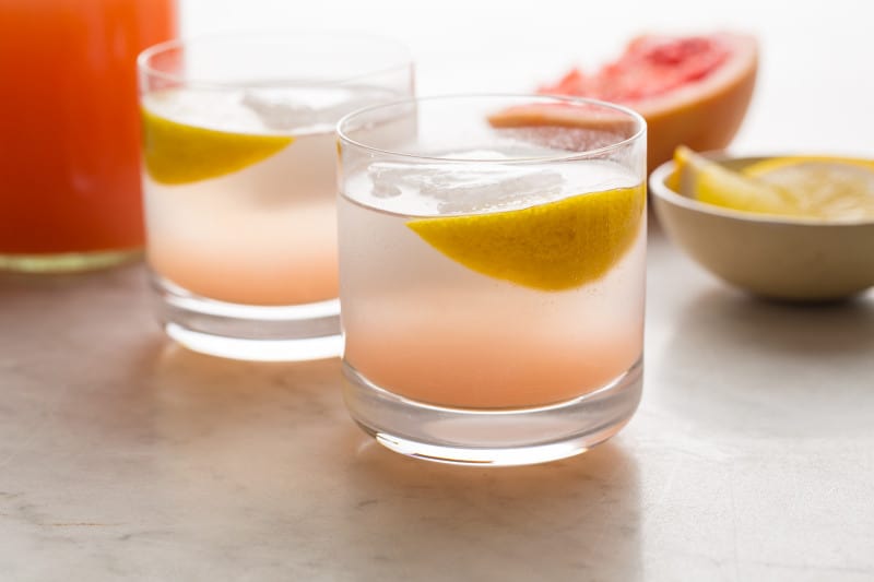 A close up of red grapefruit and rum spritzers garnished with lemon slices.