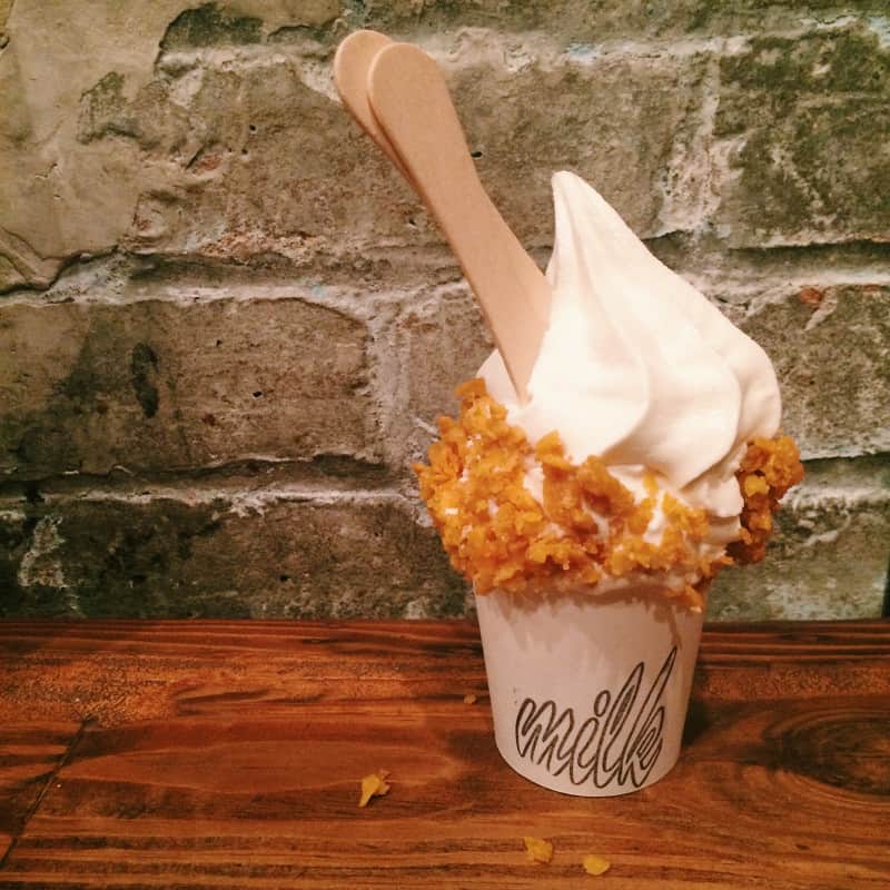 A cup of ice cream with wooden spoons on a wood table with a stone background.