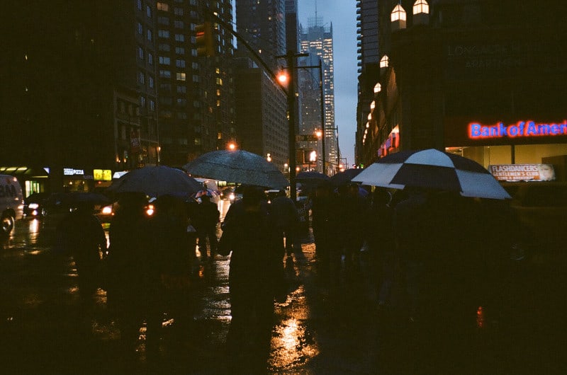 A group of people walking on a rainy night with umbrellas open.