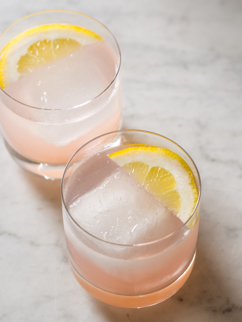 A close up of red grapefruit and rum spritzers garnished with lemon slices.