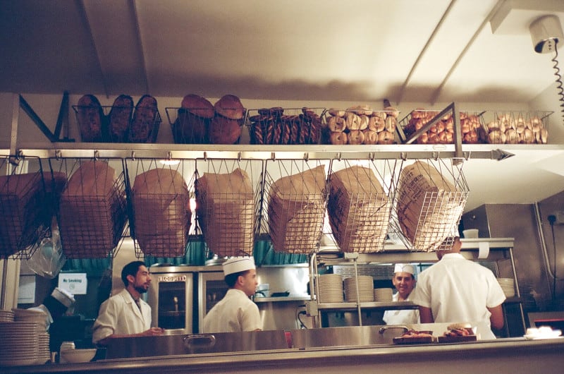 A group of cooks in a kitchen with bagels and bins above.