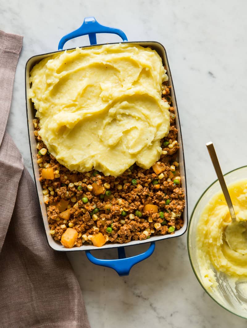 A baking pan of shepherd's pie with sweet potato being spread on top.