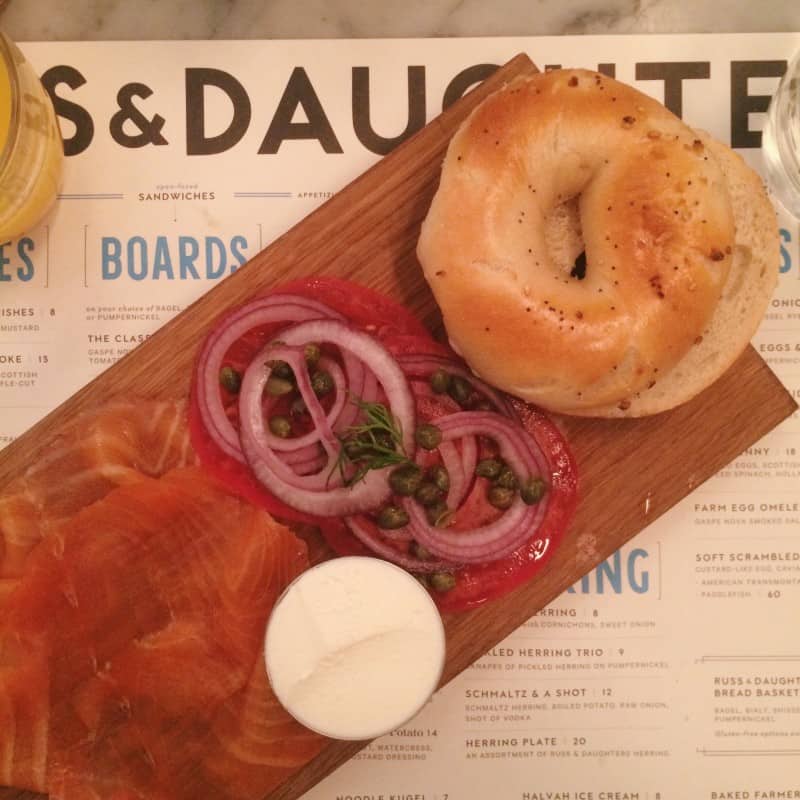 Bagel and lox on a wooden cutting board on top of a menu.