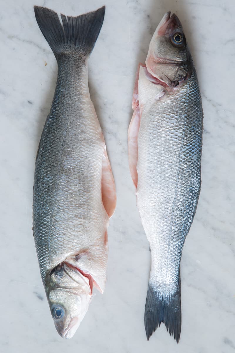 Raw whole branzino on a marble surface.