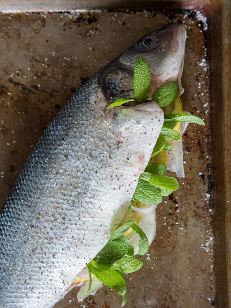 A close up of an herb stuffed raw branzino on a sheet pan.