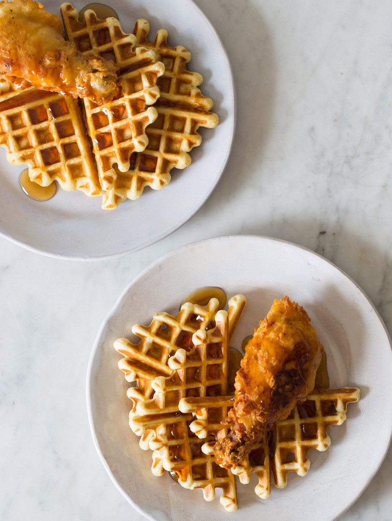 White plates of chicken and waffles on a marble countertop.