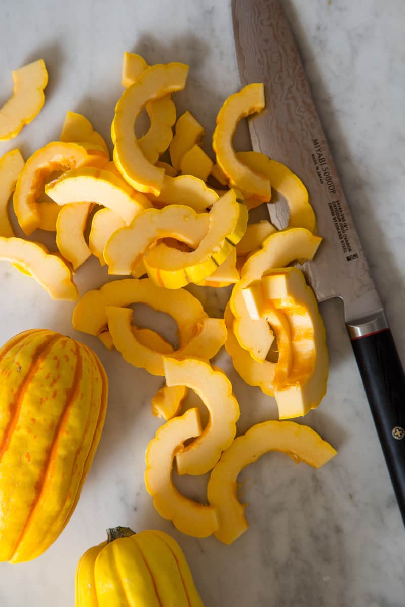 A whole and sliced delicata squash with a knife.