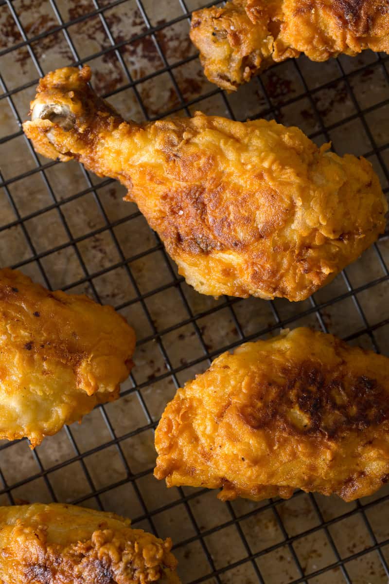 A close up of finished fried chicken drumsticks on a wire rack.