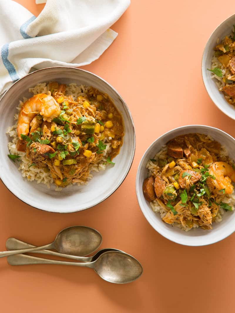 Several bowls of chicken and andouille gumbo over rice and spoons.