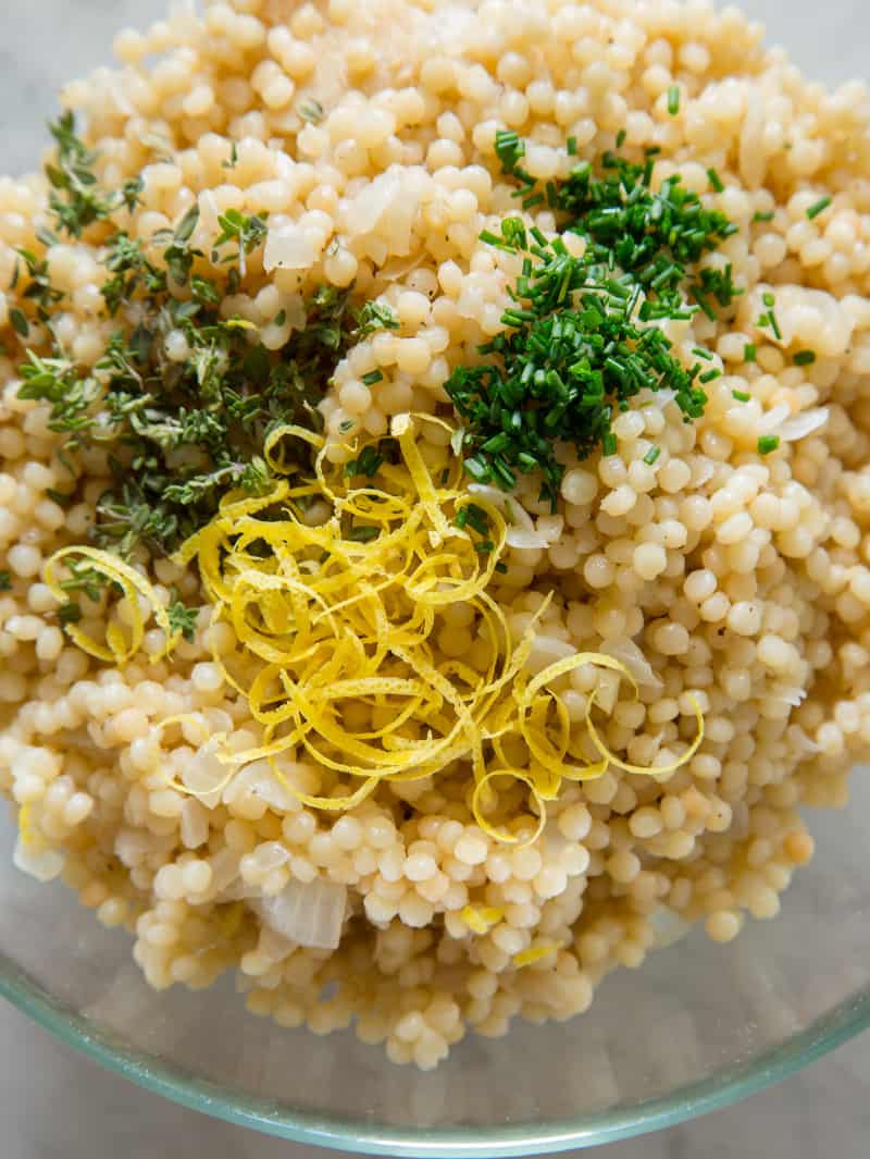A close up of Israeli couscous with herbs on top to be mixed in.