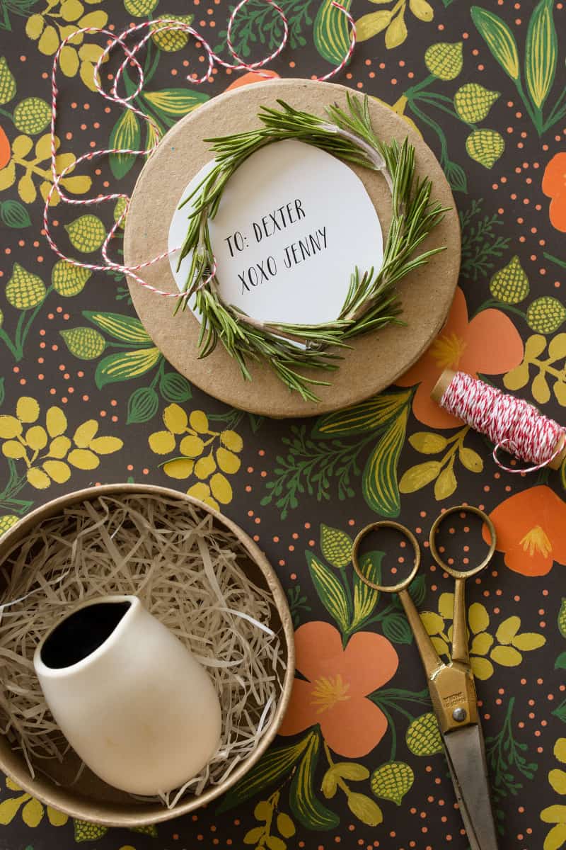 Rosemary wreath gift toppers tied to brown gift boxes with scissors and string.