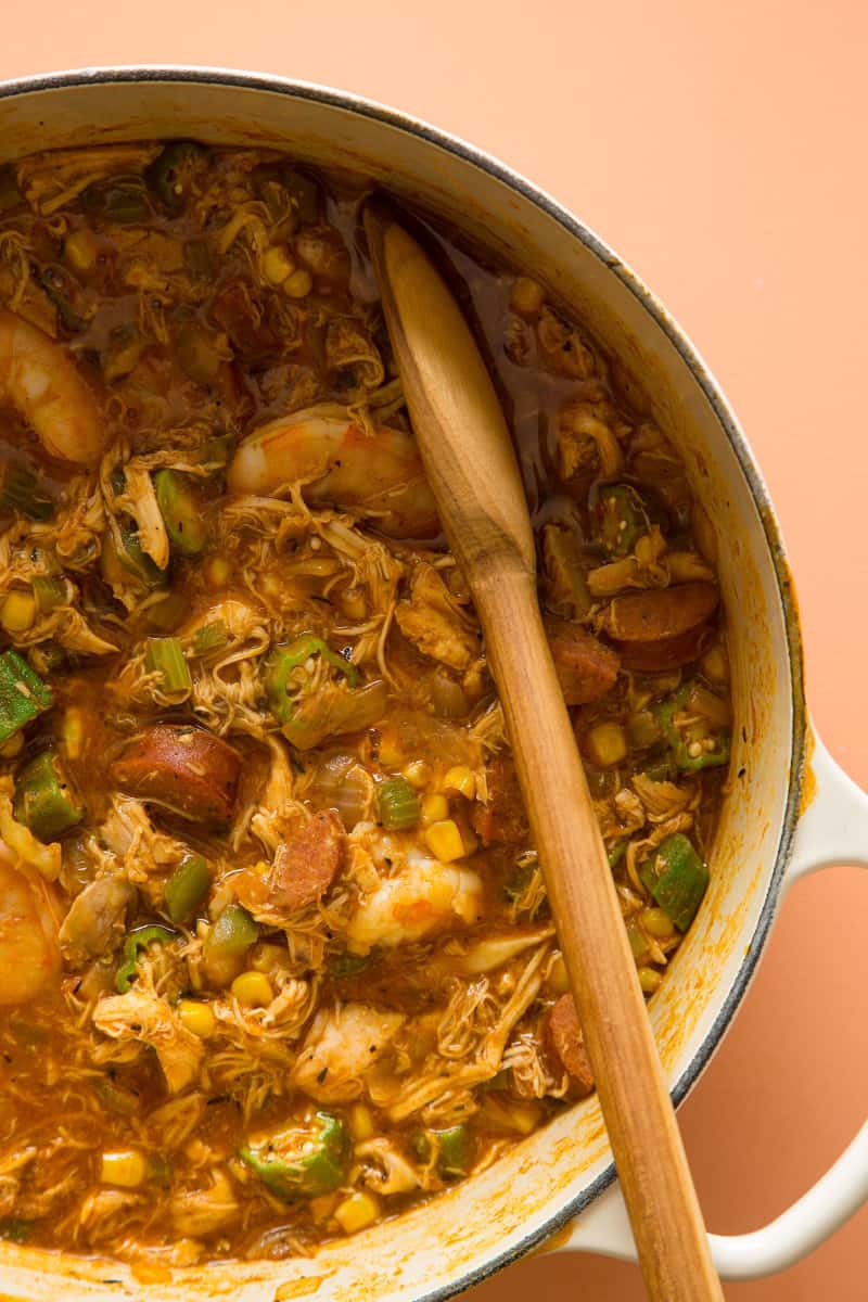 A close up of a pot of chicken and andouille gumbo and a wooden spoon.