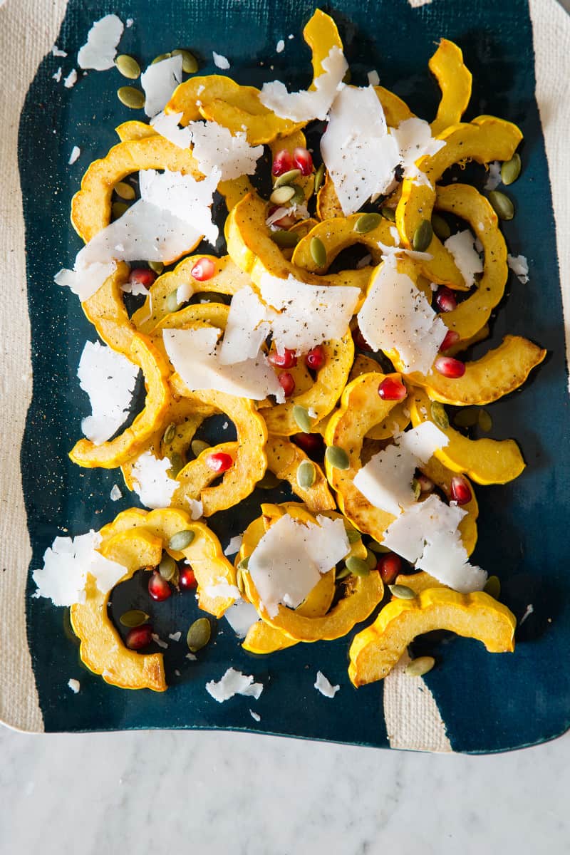 A close up of honey roasted delicata squash on a turquoise and white platter. 