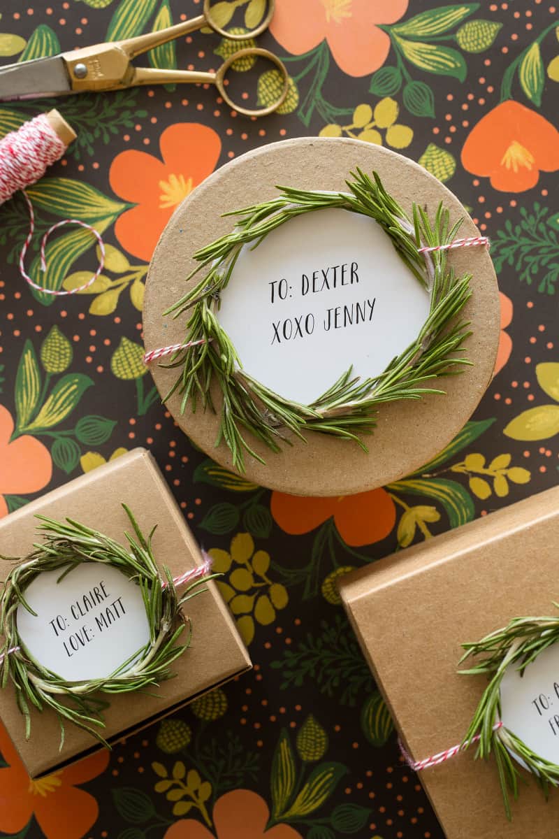 A close up of rosemary wreath gift toppers tied to brown gift boxes.