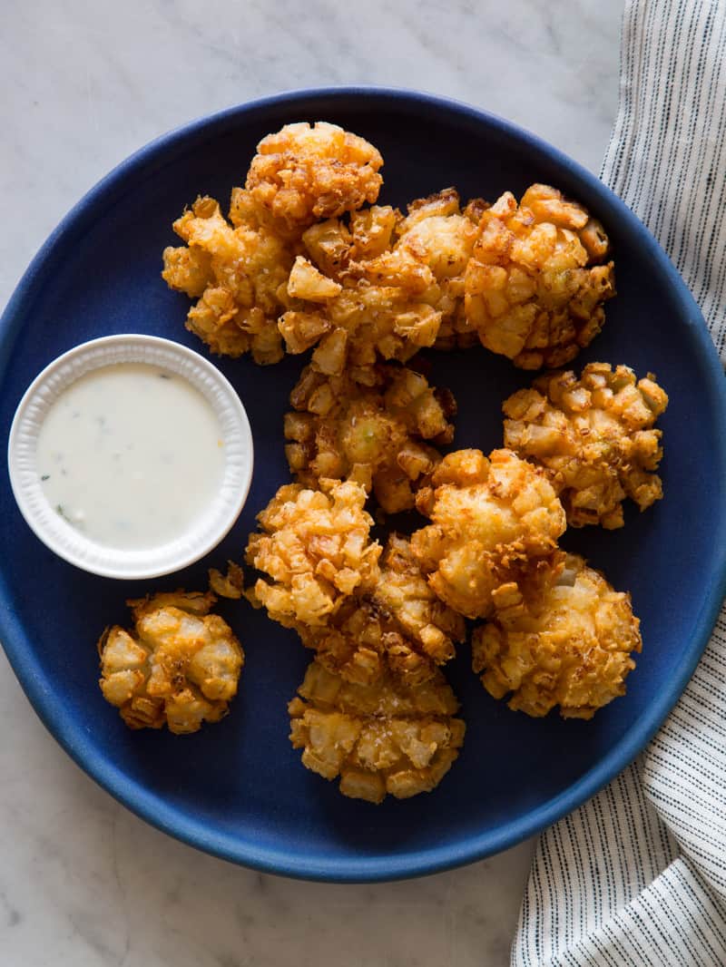 Baby bloomin\' onions on a dark blue plate with a side of buttermilk ranch dipping sauce.