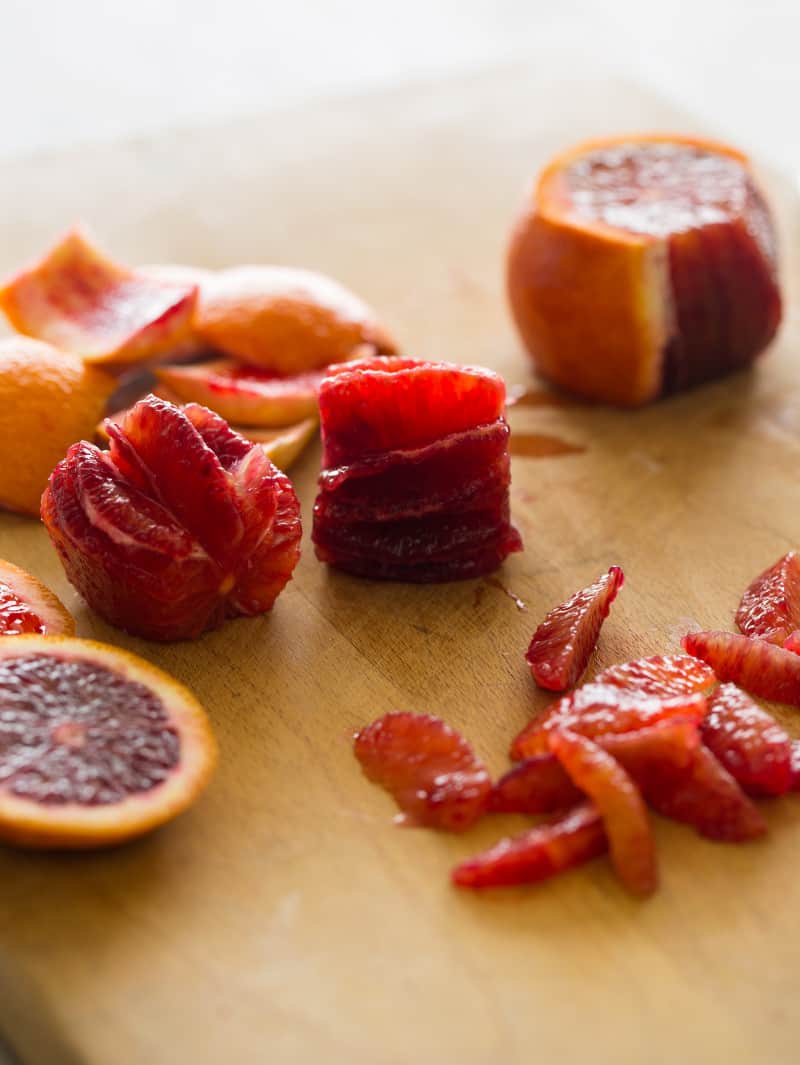 Sliced and segmented blood oranges on a wooden cutting board.