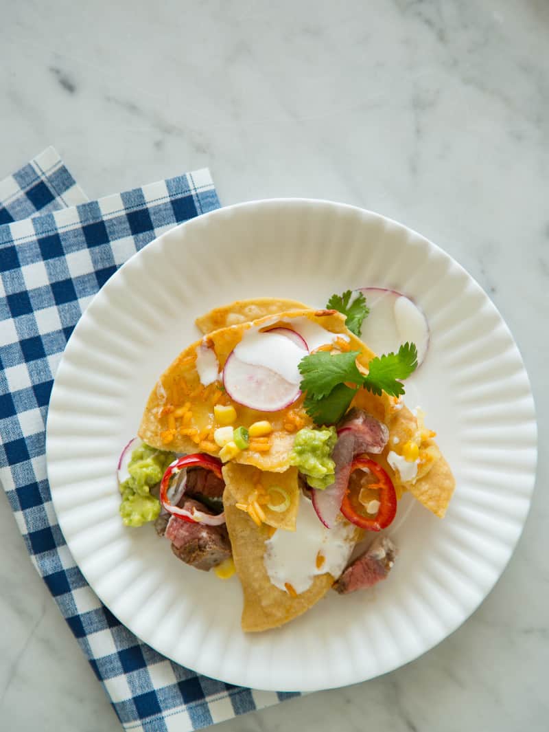 Nachos appetizer recipe A plate of carne asada nachos with a blue gingham print napkin.