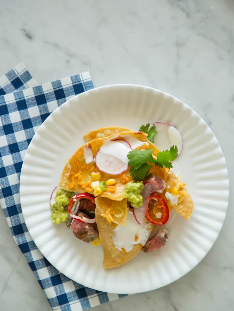 A plate of carne asada nachos with a blue gingham print napkin.