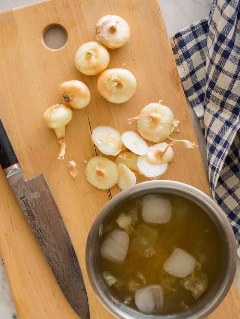 Onions soaking in water and being chopped up with a knife on a cutting board.