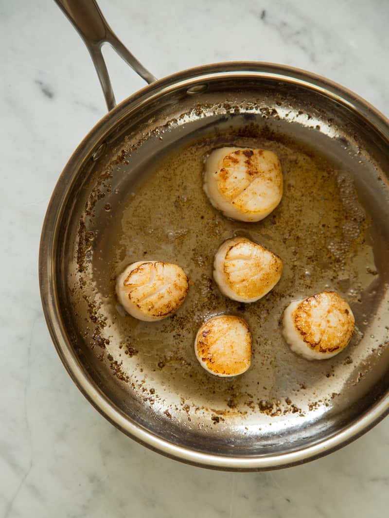 Citrus marinated scallops being seared in a frying pan.