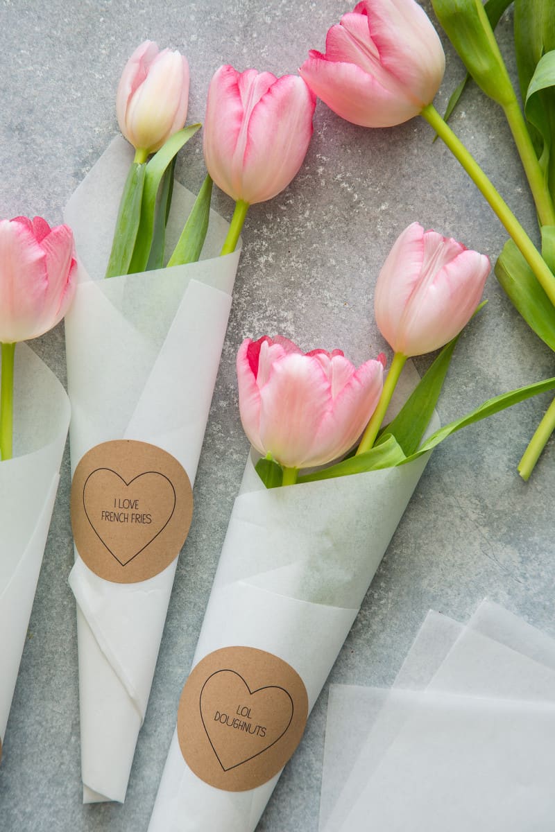Pink tulips being wrapped in paper with Valentine\'s conversation heart labels.
