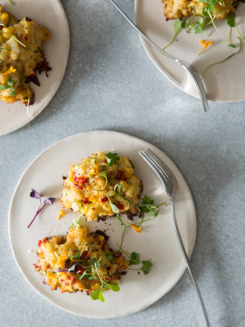 Several white plates with colorful crab cakes and forks.