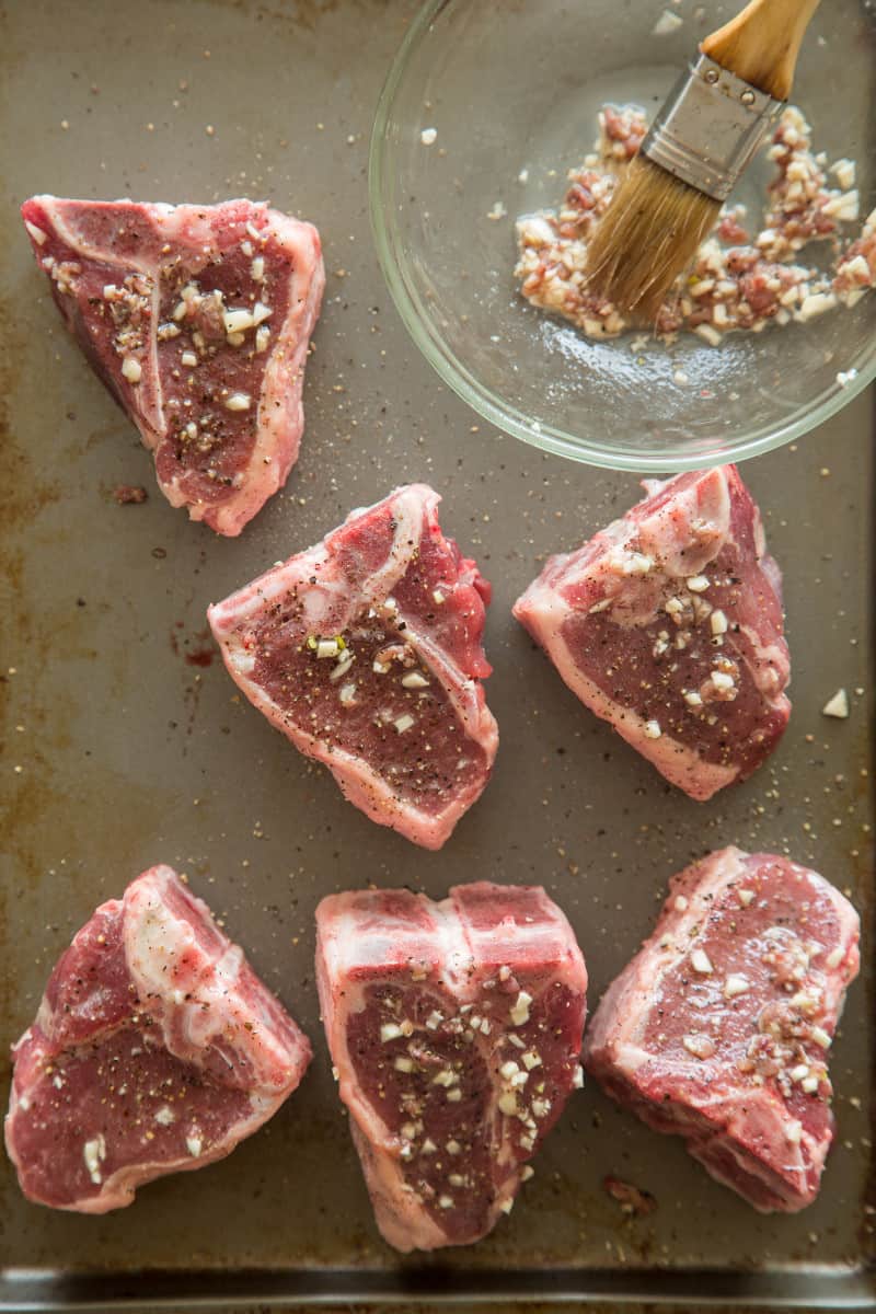 Raw lamb chops being brushed with garlic and anchovy mixture.