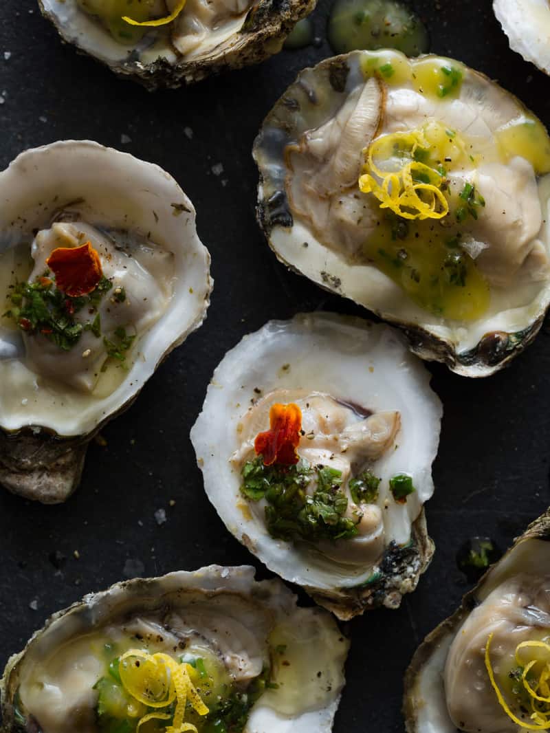 A close up of roasted oysters with a variety of garnish.