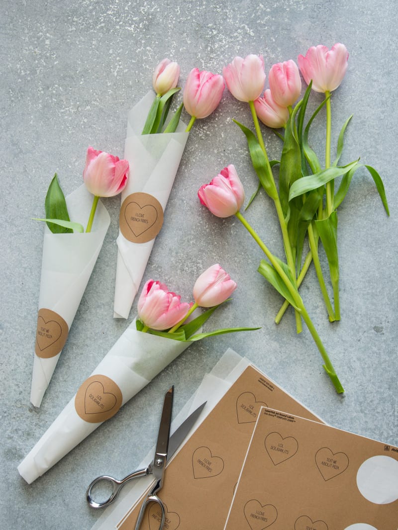 Valentine\'s conversation heart labels with pink tulips being wrapped in paper.