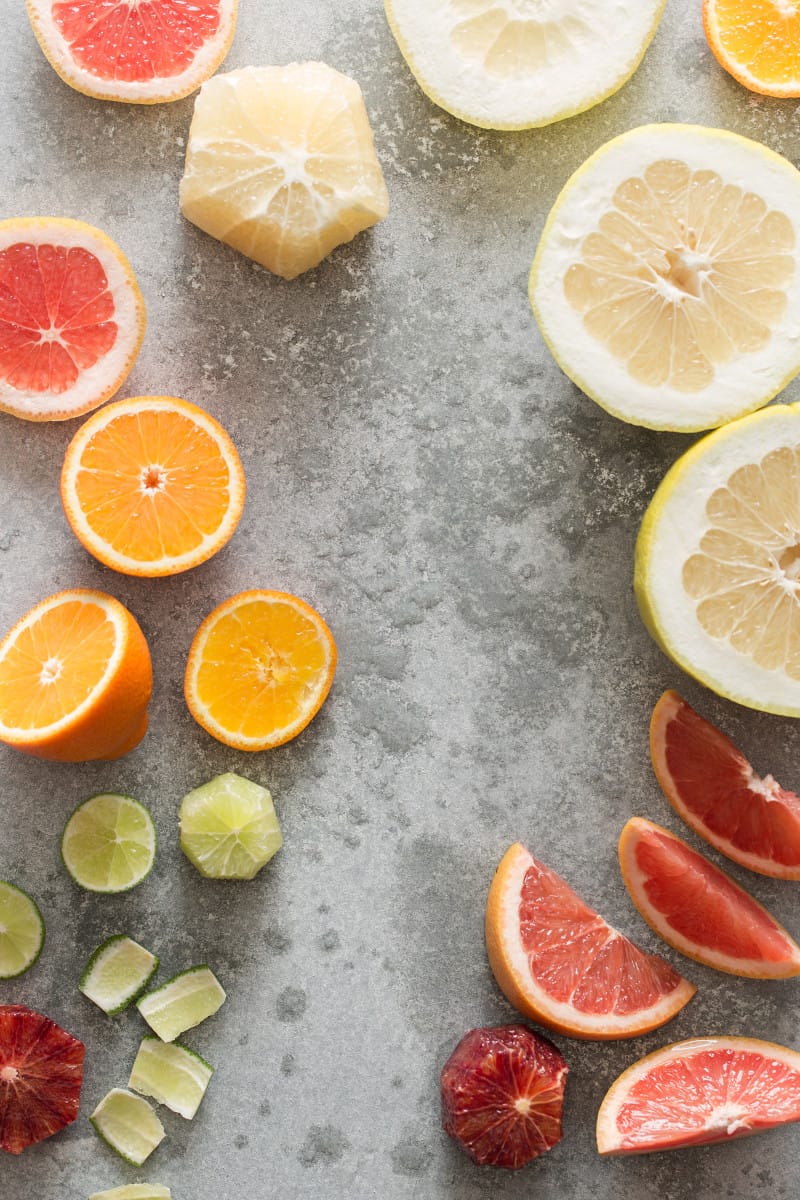 A variety of citrus cut in half and wedges on a gray surface.